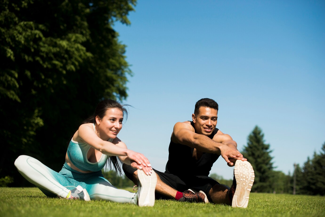 man and woman stretching on grass under a clear blue sky