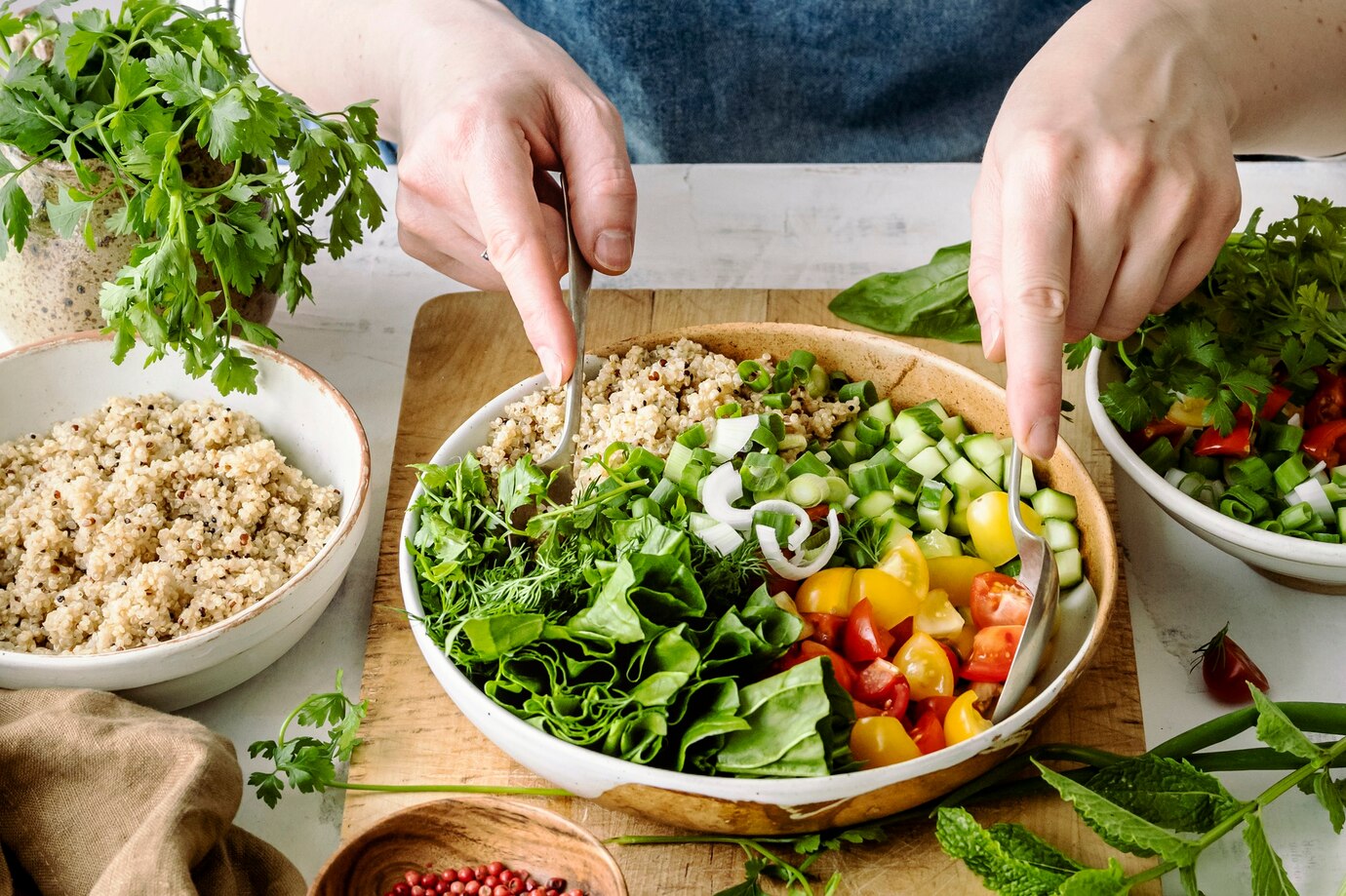 person arranges a colorful, fresh salad with ingredients like quinoa