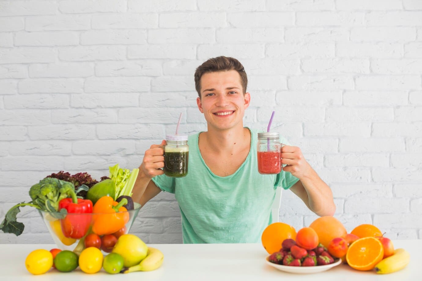 Young man smiling at the camera, holding two jars of fruit smoothies