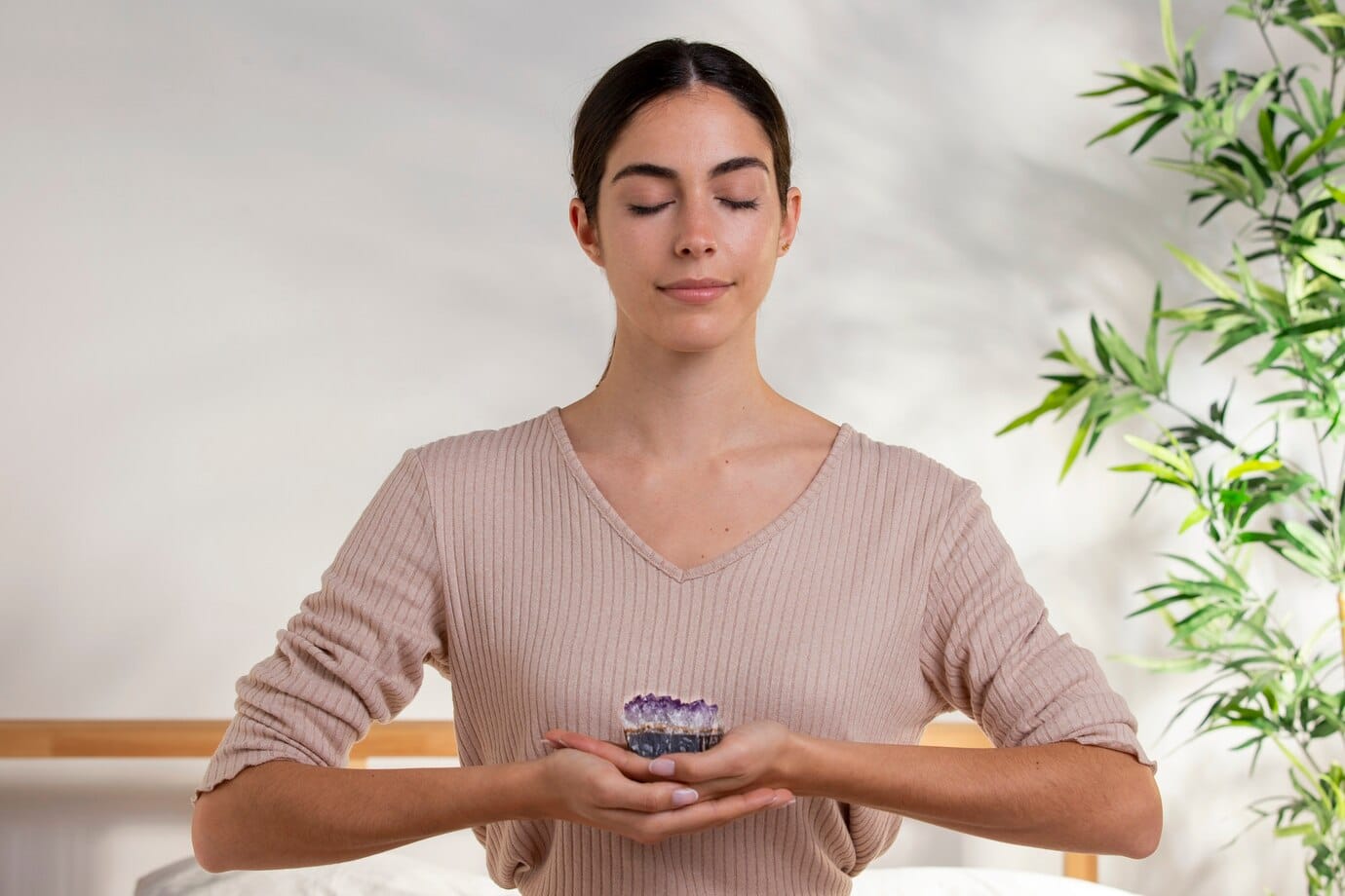 woman in a beige sweater holding a small amethyst geode
