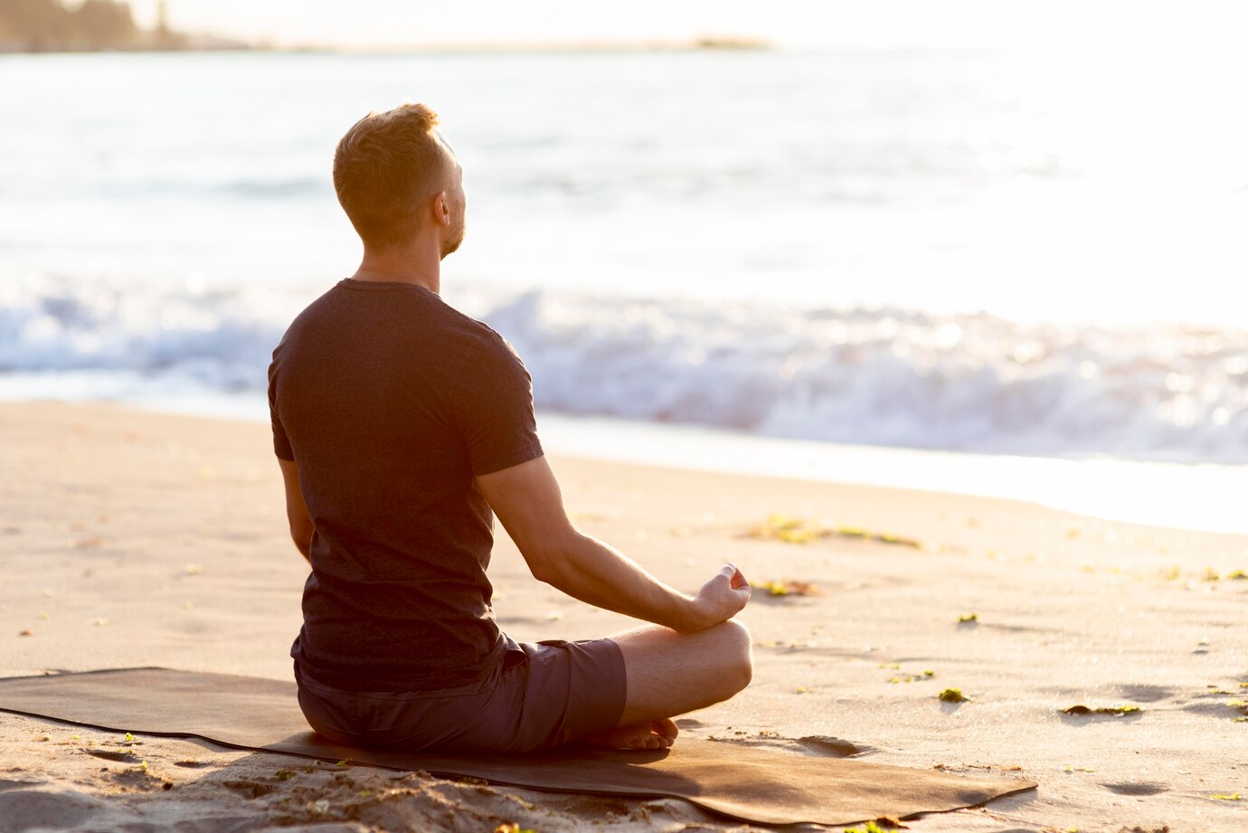 A man sits cross-legged on a beach mat, meditating peacefully