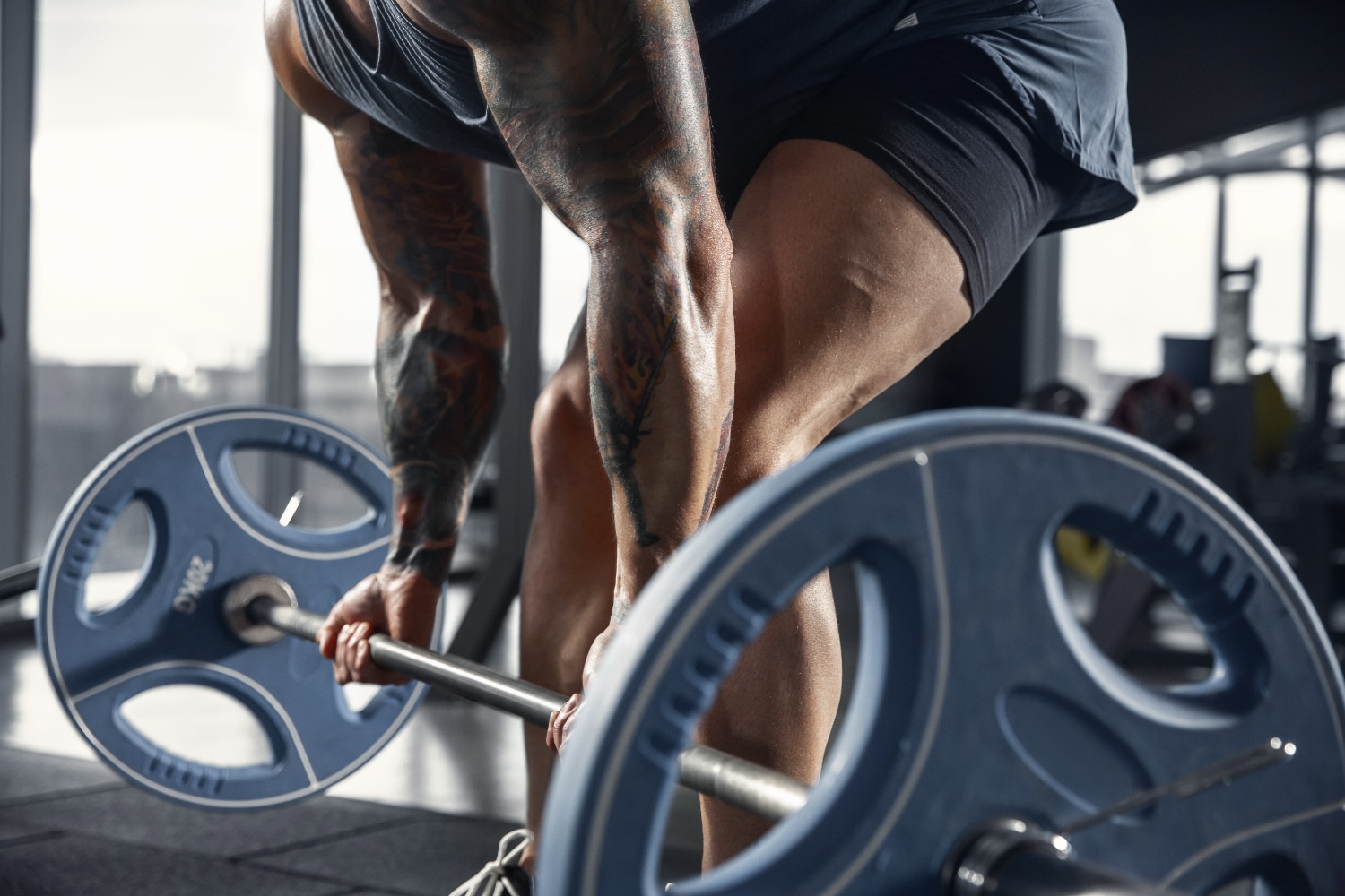 Young muscular caucasian athlete practicing pull-ups in gym with barbell.