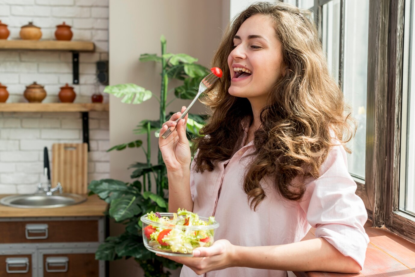  woman in a light pink shirt enjoys a fresh salad with a cherry tomato
