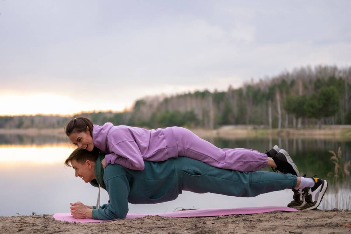 Two people performing a tandem plank exercise by a lakeside at dusk.