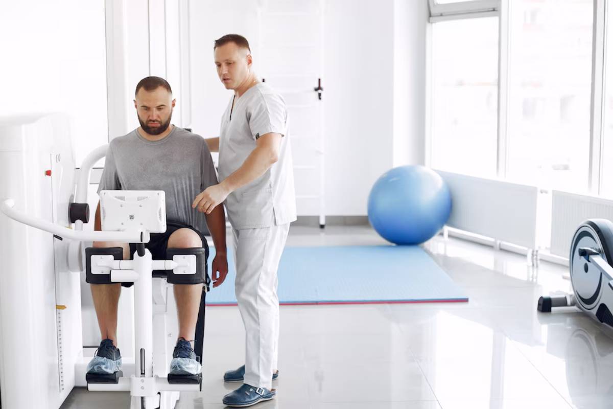 Physical therapist assisting a man with leg exercises on a rehabilitation machine in a clinic.