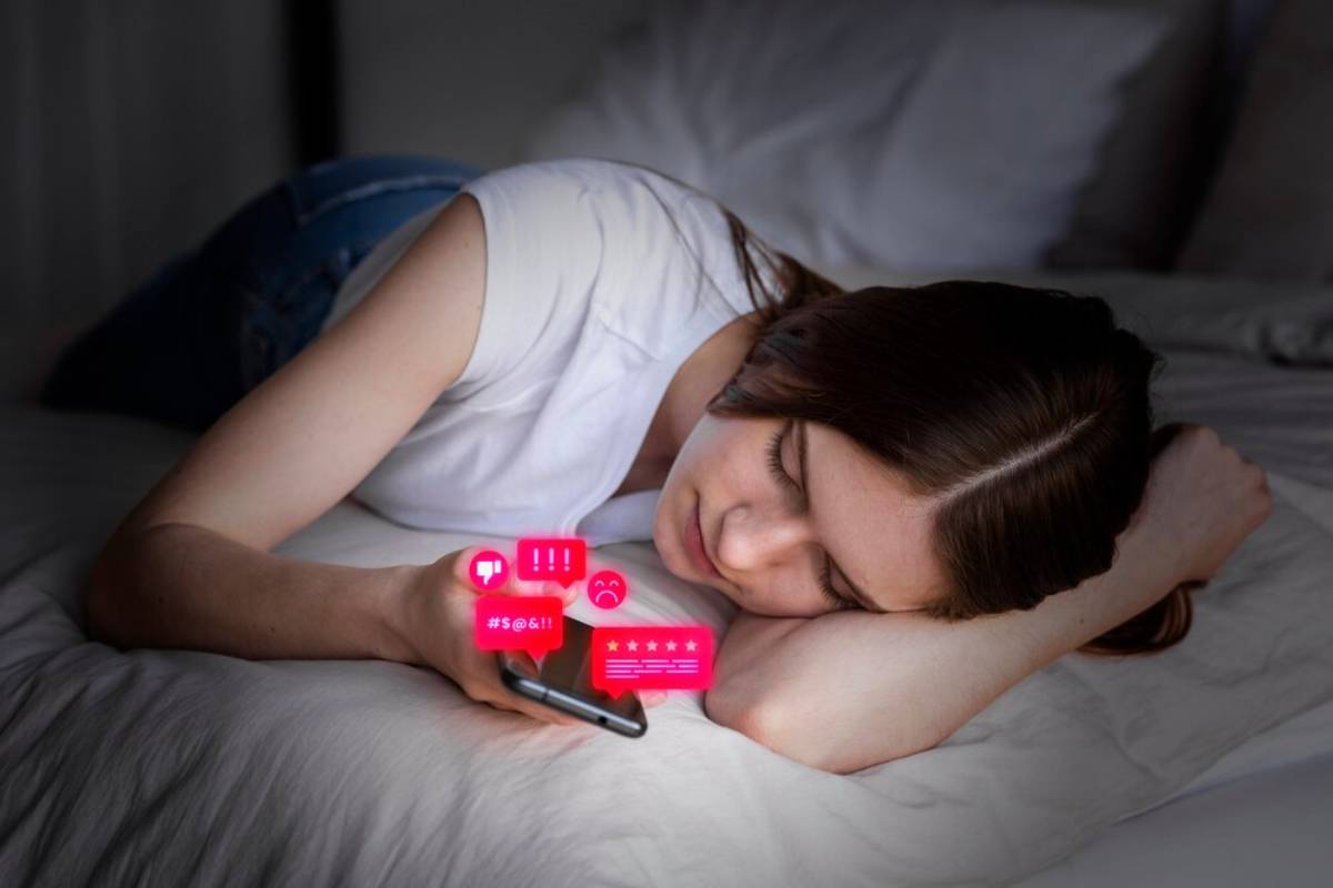 Woman lying on bed looking at smartphone with glowing social media notifications above the screen.