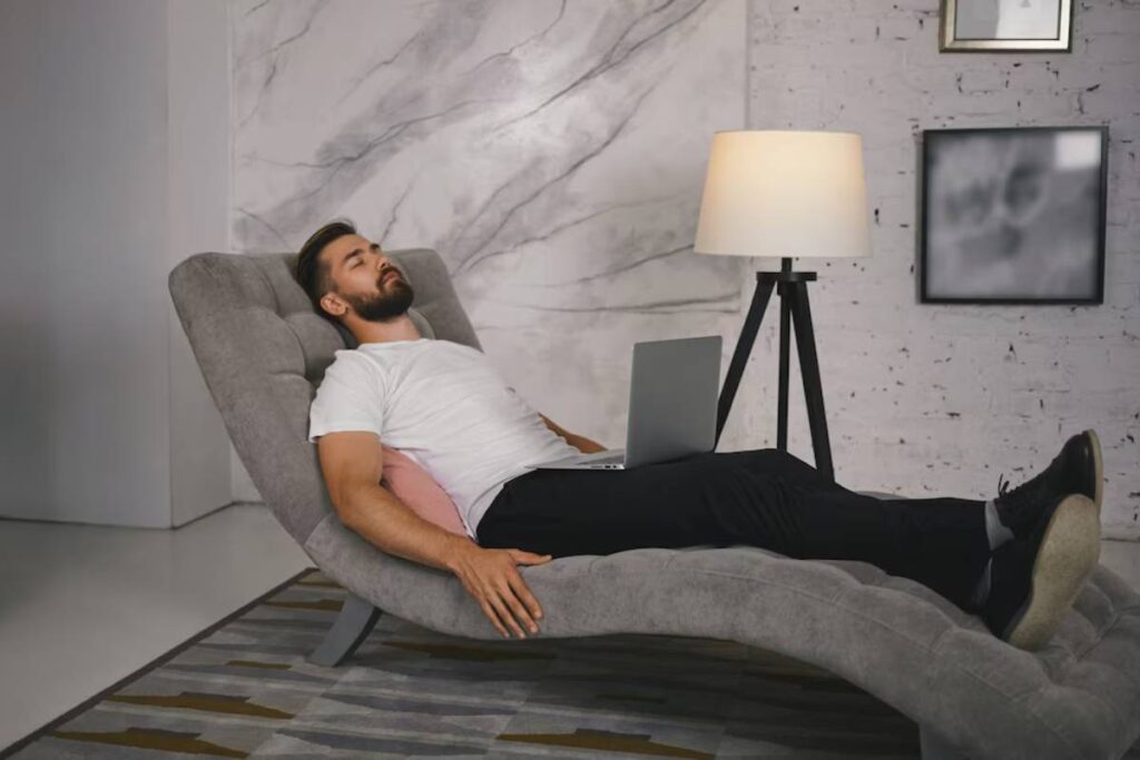 Man napping on a modern chaise lounge with a laptop on his lap in a stylish living room.