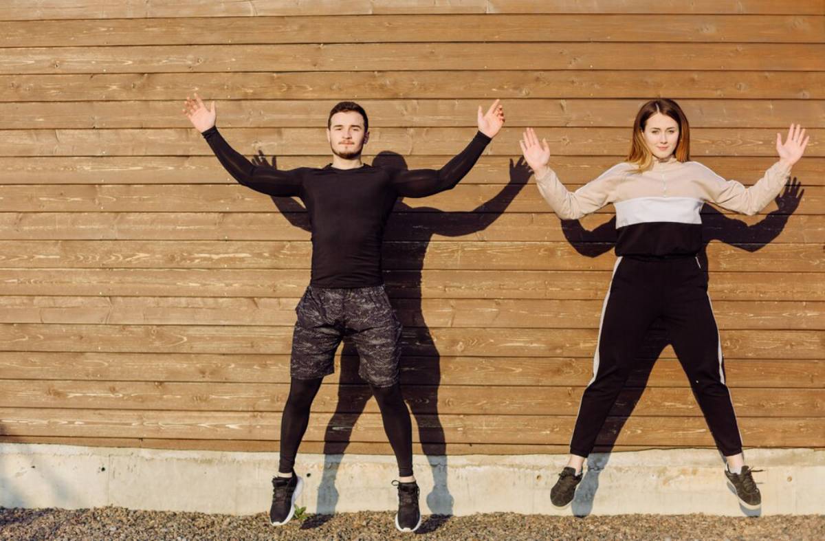 Two people jumping and posing with raised arms against a wooden wall.