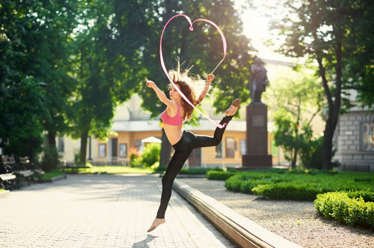 Woman dancing with a pink ribbon forming a heart shape in a sunny park.