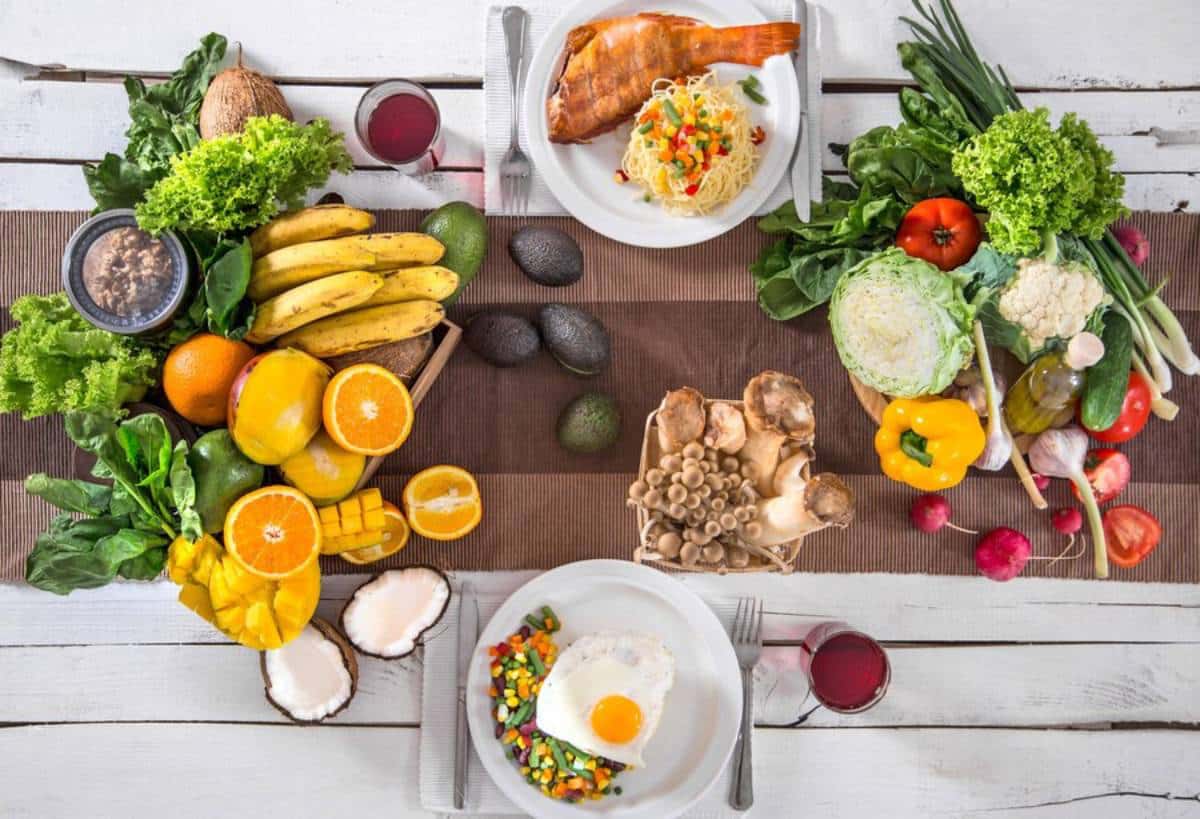 Overhead view of a healthy meal setup with fruits, vegetables, fish, and eggs on a wooden table.