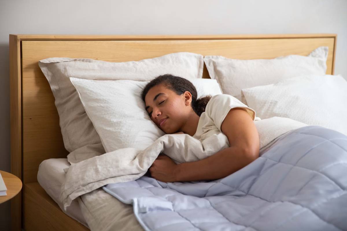 Young woman sleeping peacefully in a bed with white pillows and a light blue blanket.