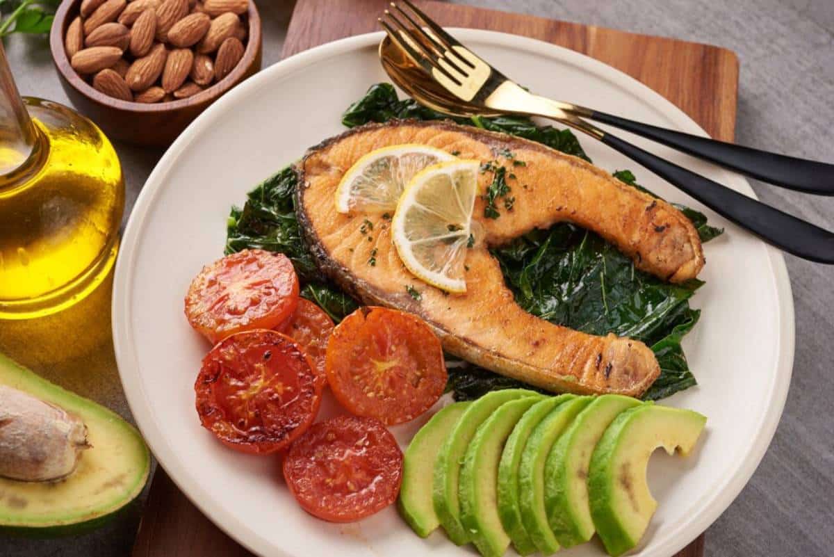 Grilled salmon with spinach, avocado, roasted tomatoes, and almonds on a dining table.